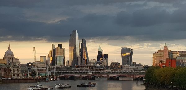 Bridge over river by buildings against sky in city