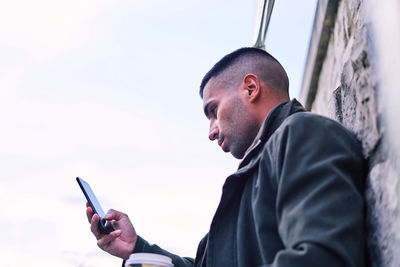 Side view of man using mobile phone against sky