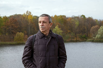 Adult retired man stands by the lake on beautiful autumn day and is resting. slowdown concept. 