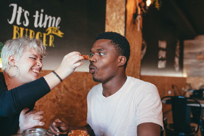 Playful woman smearing nose of black male friend with sauce while sitting in fast food cafe and having fun