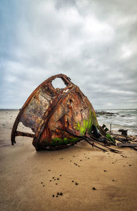 Rusty abandoned boat at beach against sky