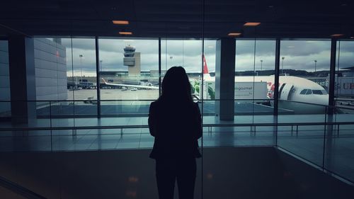 Rear view of woman standing by window at airport