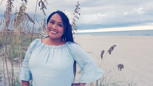 Portrait of smiling woman standing on beach against sky