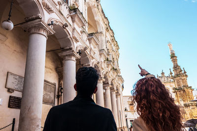 Rear view of people looking at historical building in city