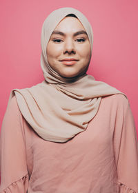 Portrait of smiling young woman wearing hijab against pink background