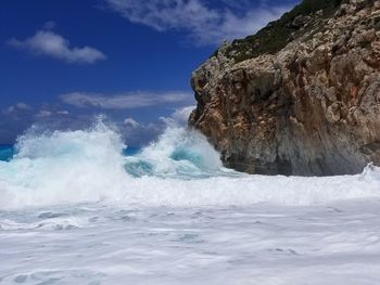 Waves breaking on rocks against sky