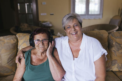 Happy woman with arm around mother sitting on sofa at home