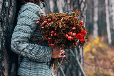 Close-up of woman holding strawberry plant against tree trunk