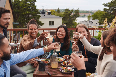 Happy friends toasting drinks while sitting on terrace