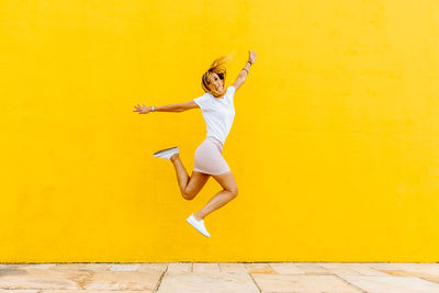 Full length of a woman jumping against yellow wall