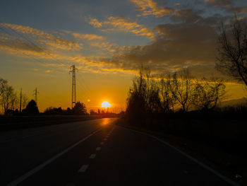 Road by silhouette trees against sky during sunset