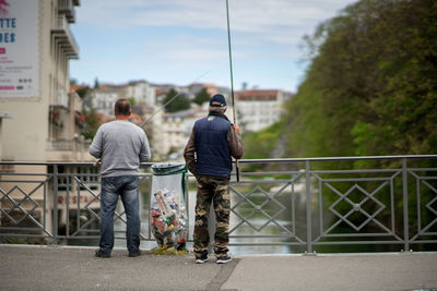 Rear view of men walking on railing against sky