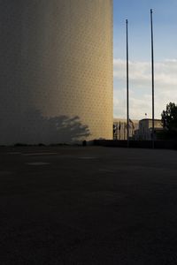 Empty road by silhouette buildings against sky