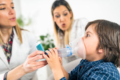 Close-up of boy inhaling medicine while doctor and mother helping