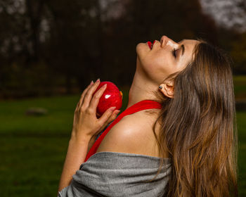 Side view of young woman holding apple