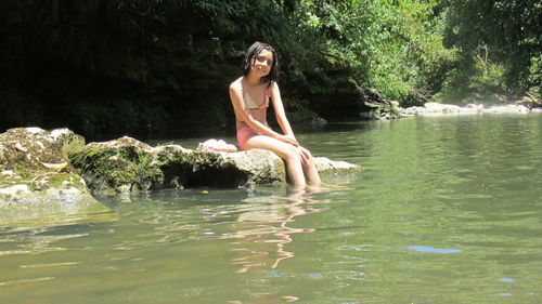 Portrait of girl wearing bikini sitting on rock in forest