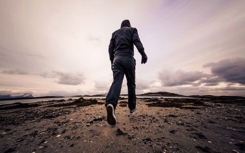 Rear view of man walking on landscape against cloudy sky