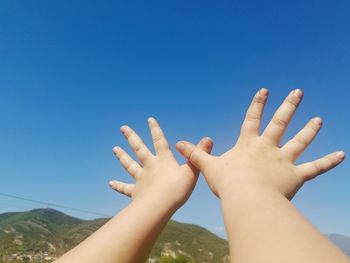 Cropped hands of child gesturing against blue sky during sunny day