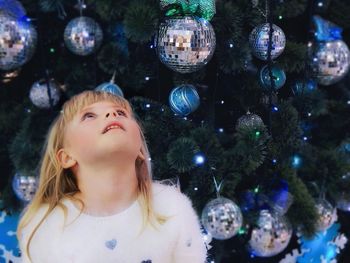 Close-up of girl looking up while standing against decorated christmas tree