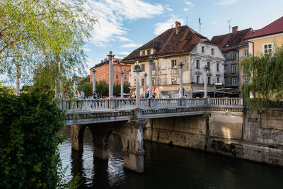 Bridge over river by buildings in city against sky