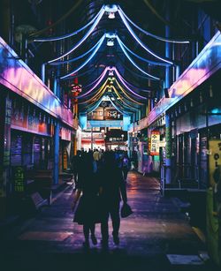 Rear view of people walking on illuminated street at night