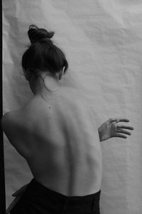 Rear view of shirtless woman standing against wall