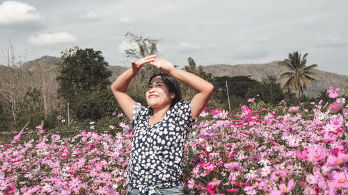 Woman standing by pink flowering plants against sky