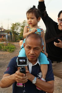 Grandfather carrying granddaughter on shoulders while photographing through camera