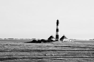 Lighthouse on field by building against clear sky