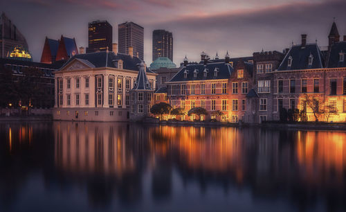 River by illuminated buildings against sky at sunset