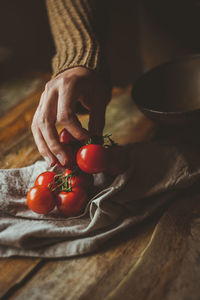 Cropped hand of woman holding cherry tomatoes on table