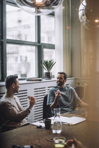 Smiling businessmen gesturing while discussing in meeting room at creative office