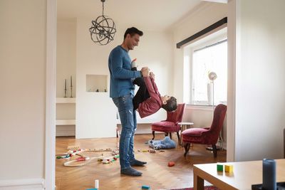 Smiling father lifting playful son while standing in living room