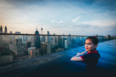 Portrait of woman in infinity pool against city