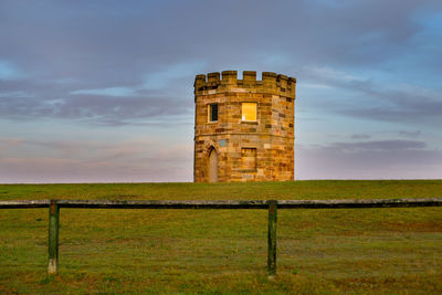 Abandoned building in field against cloudy sky