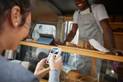 Mid adult woman using credit card reader to pay salesman at food truck