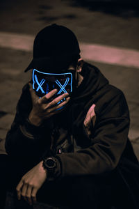 Portrait close-up of the unknown man behind the neon mask on street at night. dark brown tone