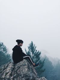 Man sitting on snow covered mountain against sky