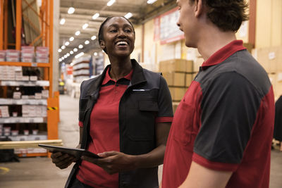 Happy saleswoman holding digital tablet while looking at male sales staff at hardware store