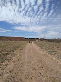 Dirt road on field against sky