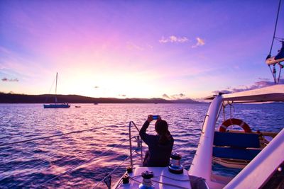 Woman photographing sea while sitting in ship during sunset