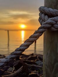 Close-up of rope tied on wooden post during sunrise