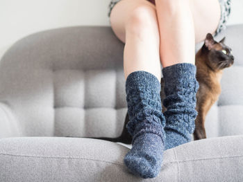 Low section of woman in socks with cat sitting on sofa at home 