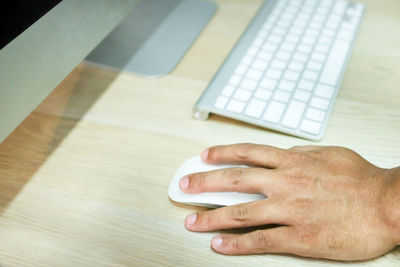 Cropped hand using computer mouse over desk in office