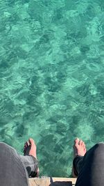 Low section of person sitting by swimming pool during sunny day