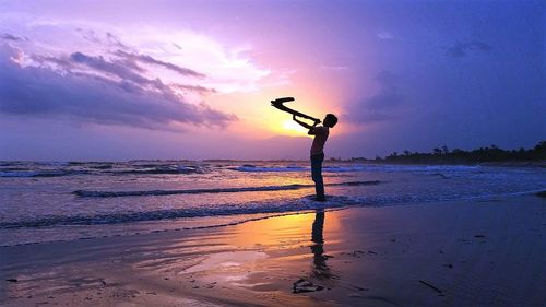 Silhouette man standing on beach against sky during sunset