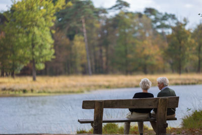 Rear view of couple sitting on bench at lakeshore