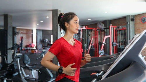 Smiling young woman running on treadmill in gym