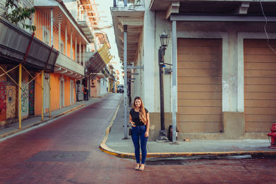 Full length portrait of woman walking on street amidst buildings