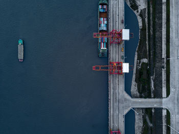 Aerial view of cranes on bridge by cargo ship over sea